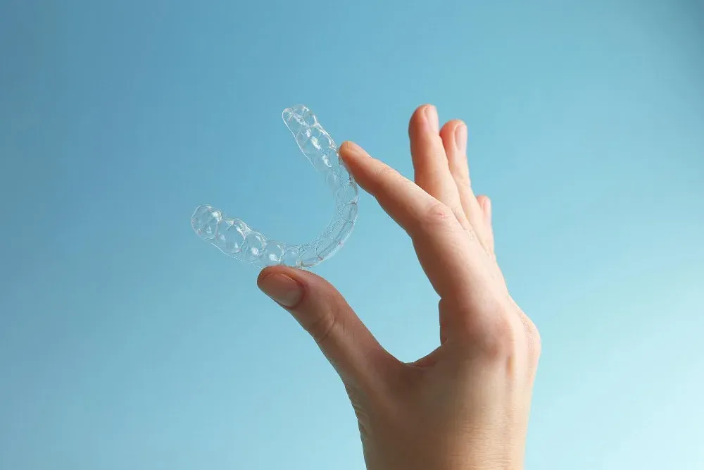 Clear aligners held by a hand against a blue backg