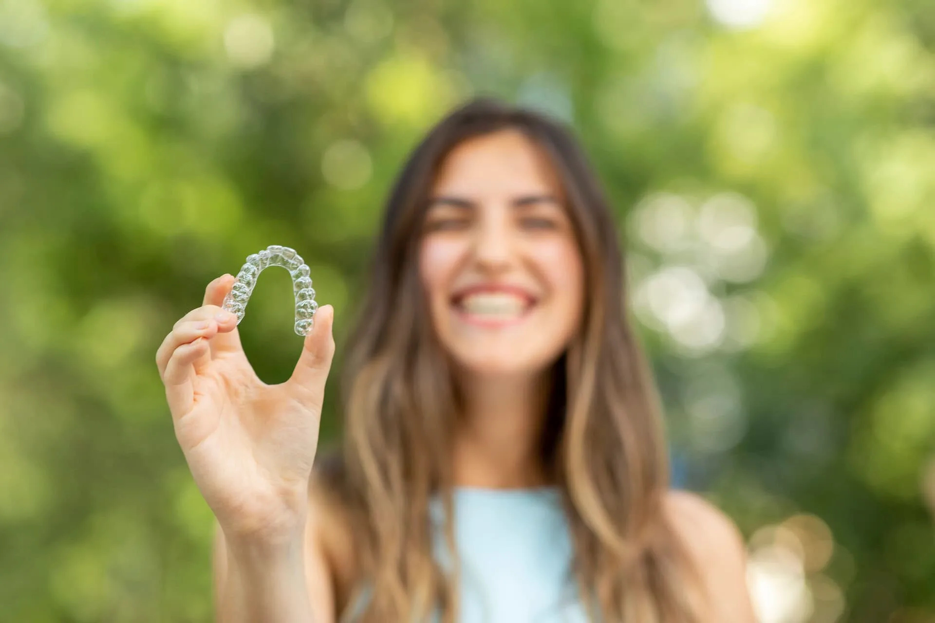 Mujer sonriente sosteniendo un alineador transparente Invisalign en Neola Dental en Minneola, FL
