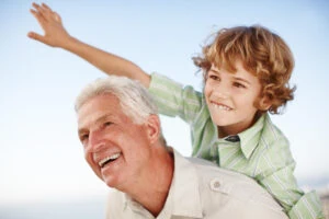 Grandfather and grandson smiling and playing outdoors on a sunny day, showcasing family bonding and happiness.