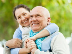 Smiling woman hugging an elderly man outdoors, showcasing family happiness and health.