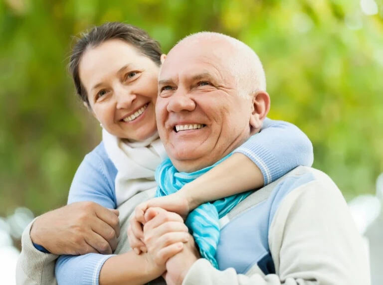 Smiling woman hugging an elderly man outdoors, showcasing family happiness and health.