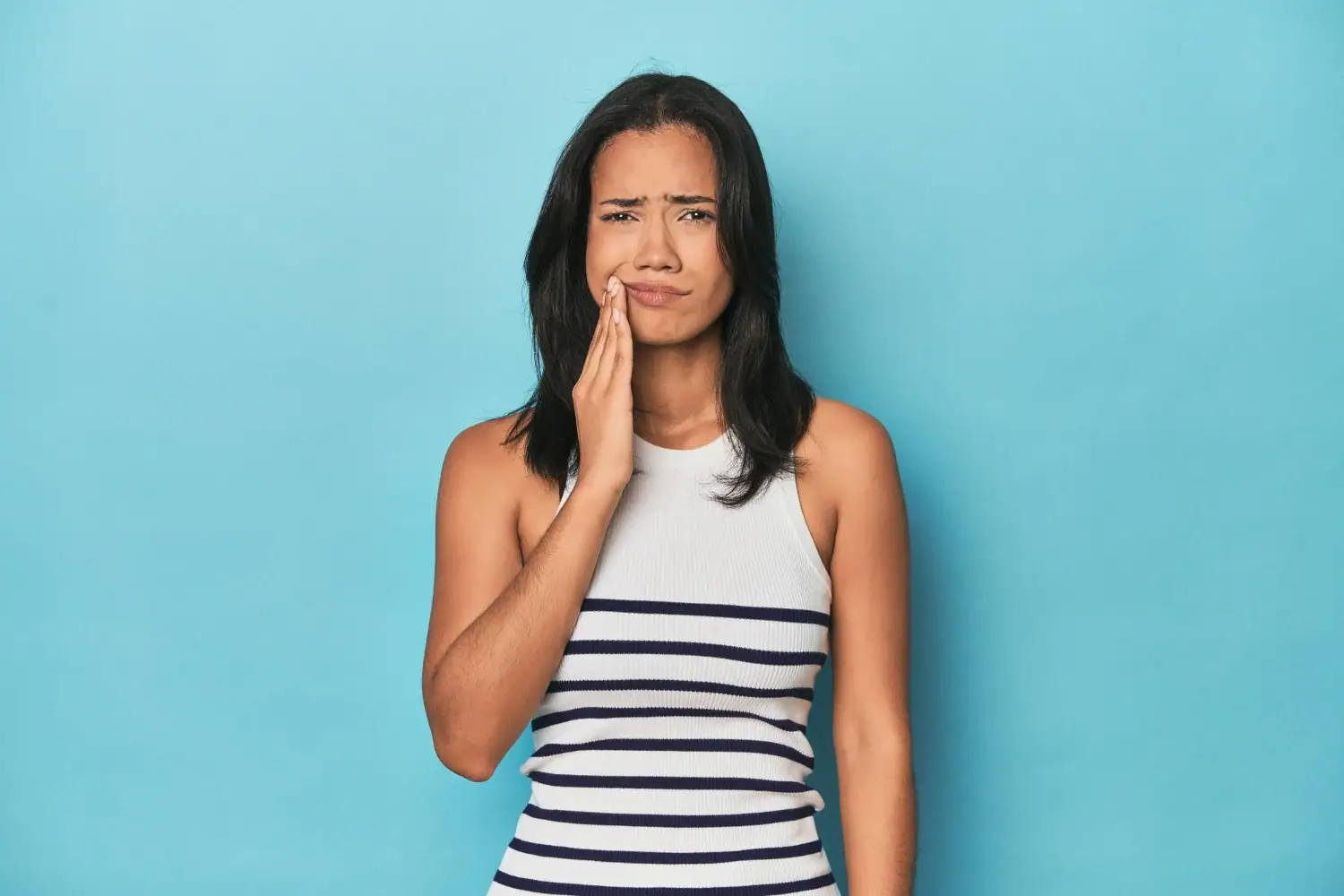 Woman experiencing tooth pain holding her jaw - dental emergency symptoms