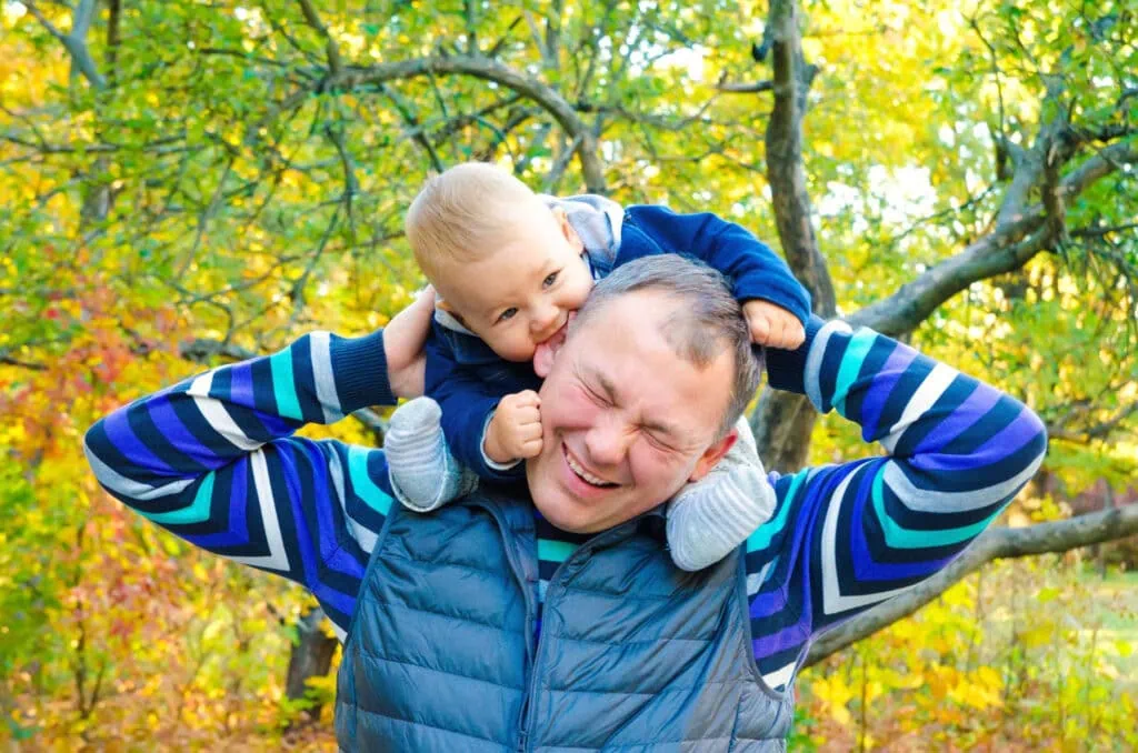 Happy father and young son playing on his shoulders in a park during autumn.