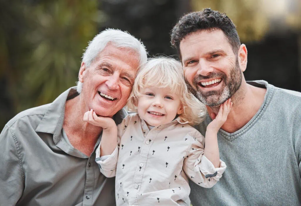 Happy family with grandparents, father, and young daughter smiling outdoors.