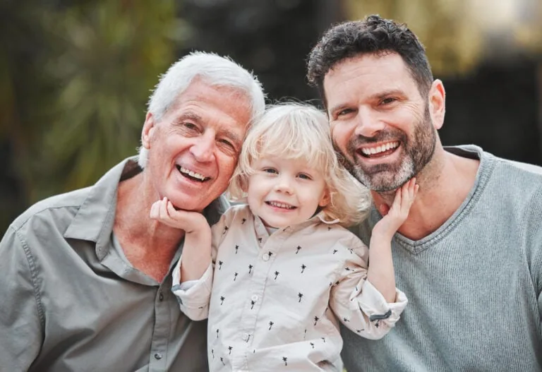 Happy family with grandparents, father, and young daughter smiling outdoors.